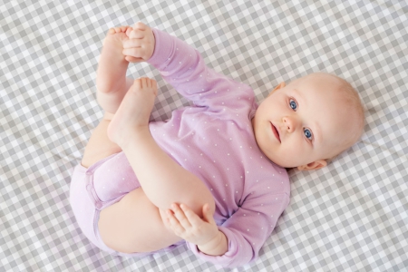 Bebé tocándose un pie sobre sábana mini cuna y capazo cuadro vichy gris. Tejido 100% algodón orgánico. Estrellita la Valiente.