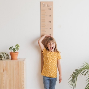 Niña midiéndose con el medidor infantil de Estrellita la Valiente. Niña midiéndose 120 cm con un medidor de madera.