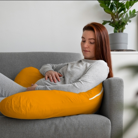 Mujer embarazada sentada en el sofá sobre un cojín de lactancia mostaza Estrellita la Valiente.