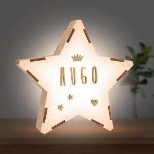 Lámpara personalizable quitamiedos tamaño Junior Hugo Estrellita la Valiente. Lámpara con forma de Estrella y el nombre de Hugo con una corona, dos estrellas y un corazón. encendida sobre una mesita de noche.