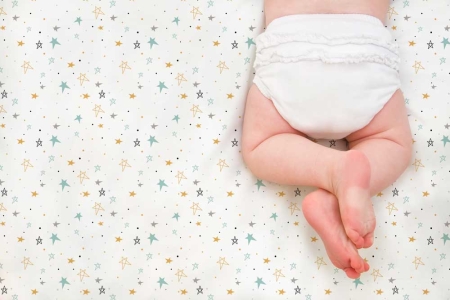 Bebé sobre sábana noche estrellada mostaza Estrellita la Valiente. Bebé boca abajo sobre uno de los juegos de minicuna y capazo Noche estrellada mostaza.