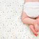 Bebé sobre sábana noche estrellada mostaza Estrellita la Valiente. Bebé boca abajo sobre uno de los juegos de minicuna y capazo Noche estrellada mostaza.