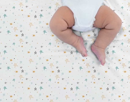Bebé tumbado boca arriba sobre sábana noche estrellada mostaza Estrellita la Valiente. Bebé boca arriba sobre uno de los juegos de minicuna y capazo Noche estrellada mostaza.