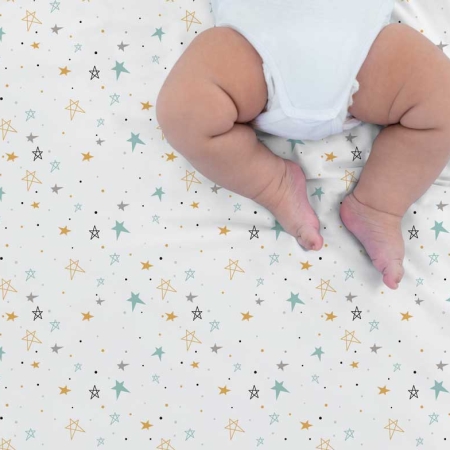 Bebé tumbado boca arriba sobre sábana noche estrellada mostaza Estrellita la Valiente. Bebé boca arriba sobre uno de los juegos de minicuna y capazo Noche estrellada mostaza.