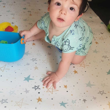 Alfombra infantil vinílica rectangular estrellas multicolor mint y mostaza con bebé. Alfombra de bebé e infantil de la tienda online de textil hogar, accesorios y decoración infantil con confección propia en la Comunidad Valenciana. Diseños propios con tejidos 100% algodón orgánico, hechos en España, sostenibles y ecológicos. Fácil de barrer y de fregar