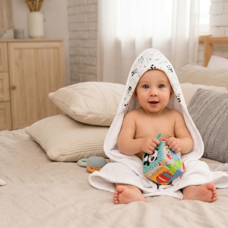 Bebé con capa de baño Panda sentado sobre cama. Capa de baño con estampado de osos panda