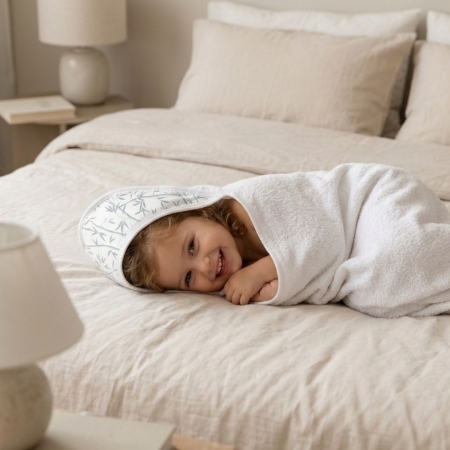 Niña con capa de baño Bambú tumbada sobre cama. Capa de baño o toalla con capucha con estampado Bambú